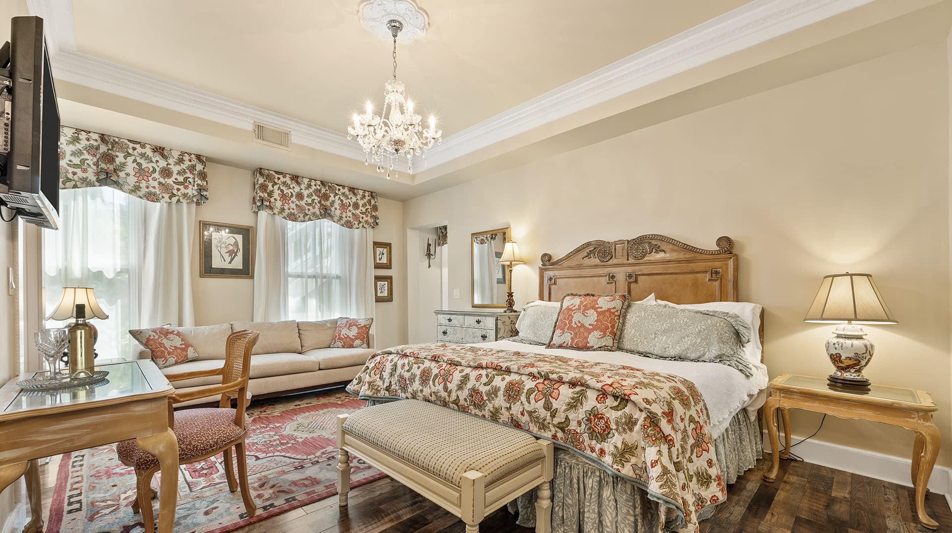A beautifully decorated bedroom featuring a floral-patterned bedspread, elegant furnishings, and ample natural light.