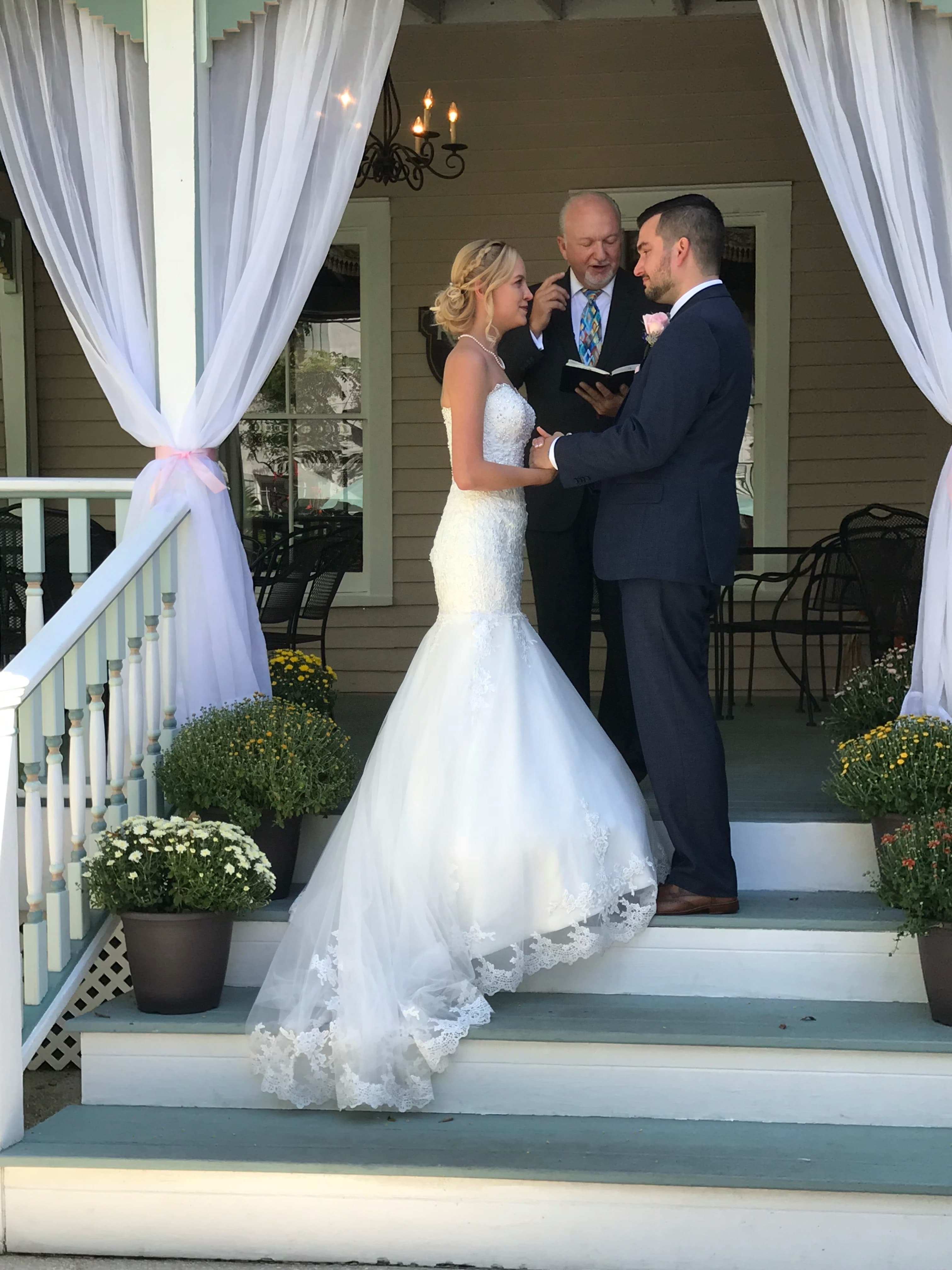 A bride and groom exchange vows outdoors, while an officiant stands between them.