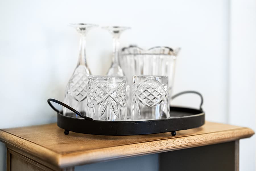 A black tray holds various crystal glasses and a decanter on a wooden surface.