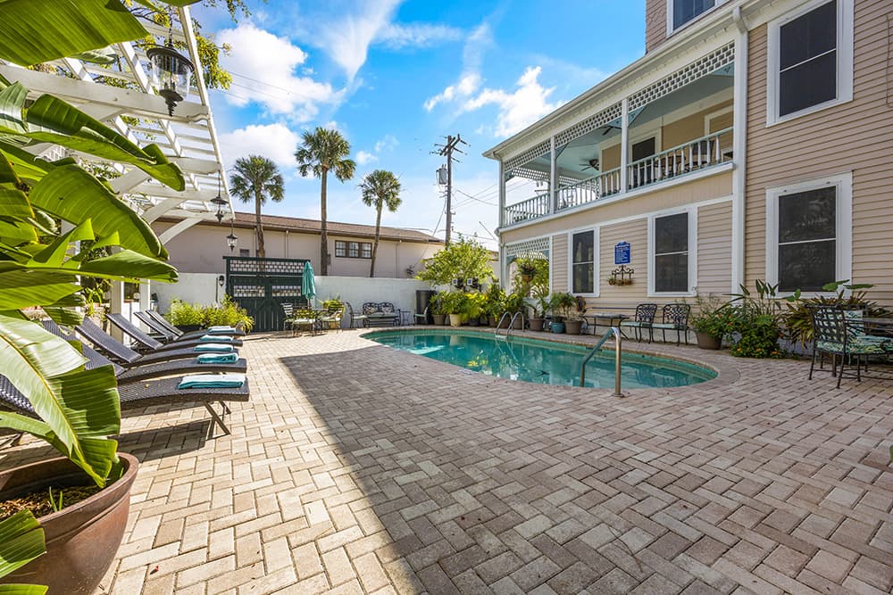 A tranquil pool area surrounded by lounge chairs and lush greenery near a yellow house.